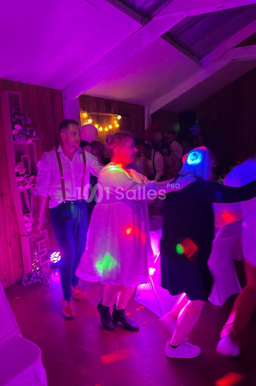 Des personnes dansent en file sous des lumières colorées dans une salle décorée pour une fête.