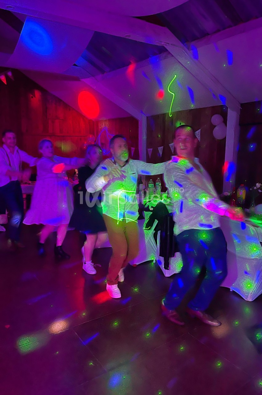 Des personnes dansent en file sous des lumières colorées dans une salle décorée pour une fête.