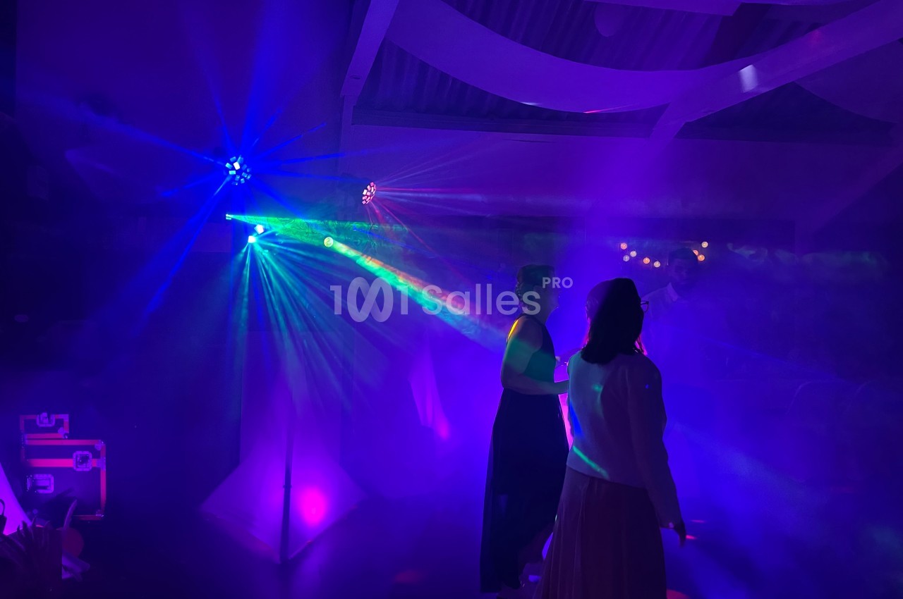 Personnes dansant sous des lumières colorées et des effets de fumée dans une ambiance festive en intérieur.