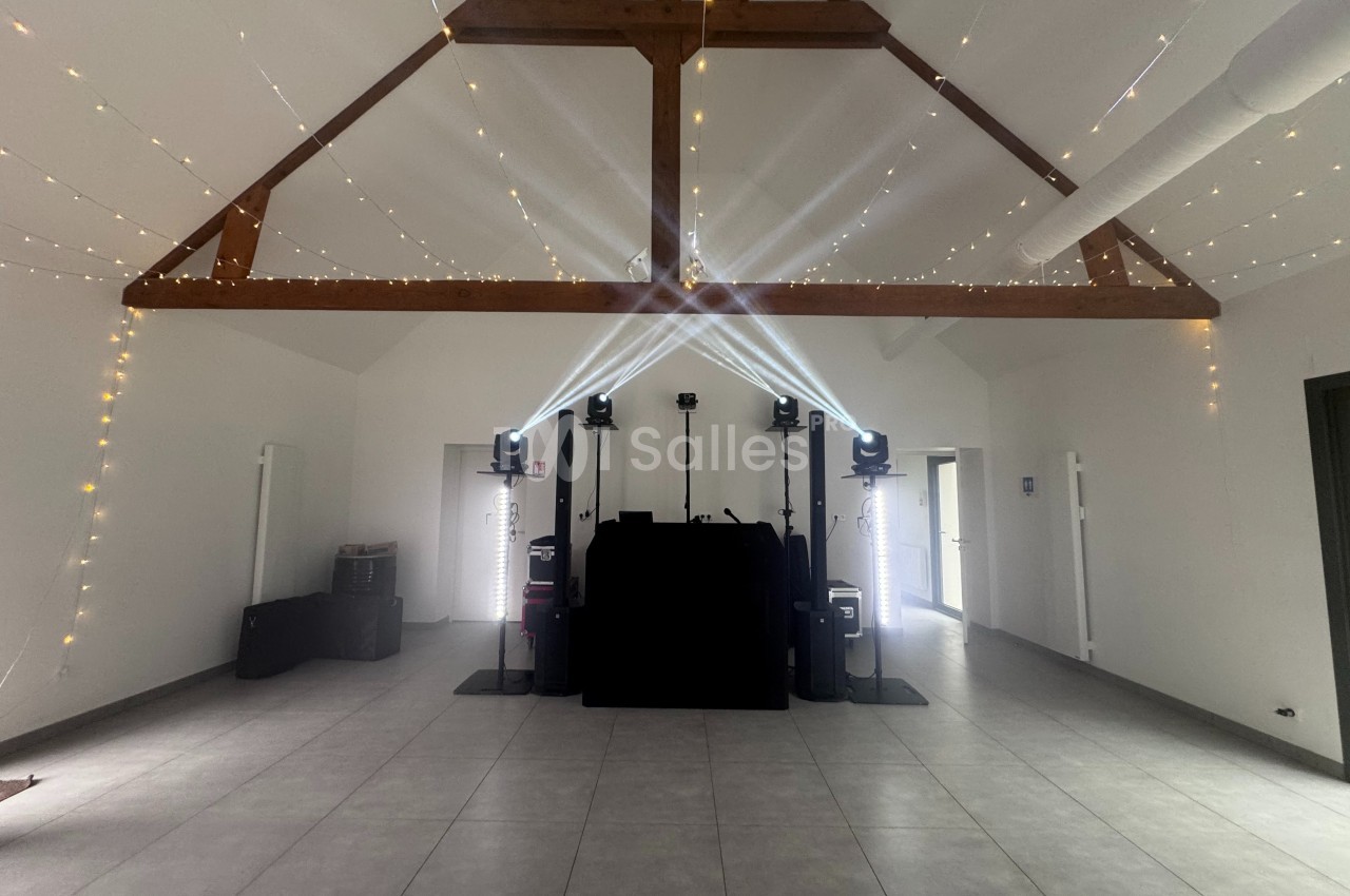 Salle avec poutres apparentes, éclairage de fête, équipements de sonorisation et guirlandes lumineuses suspendues.