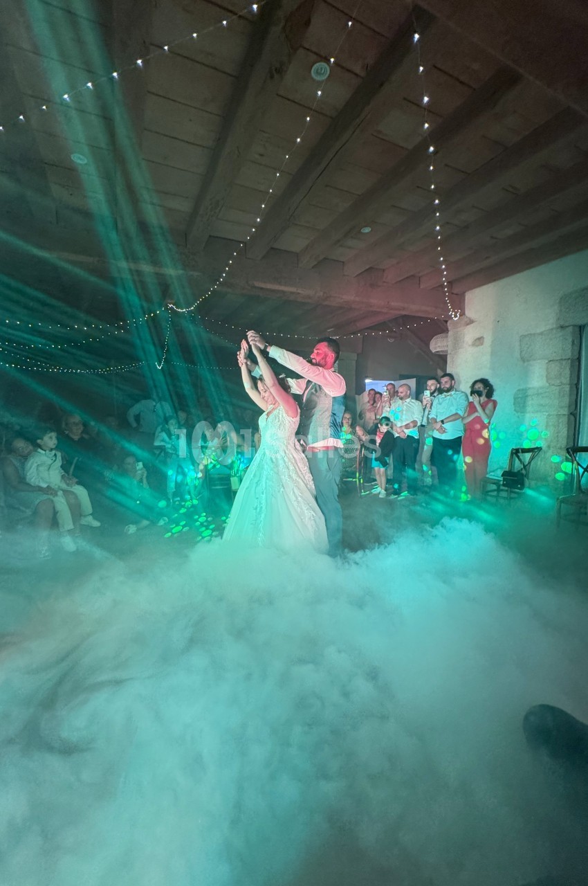 Un couple danse sous des lumières colorées et des effets de fumée, entouré d'invités dans une salle festive.