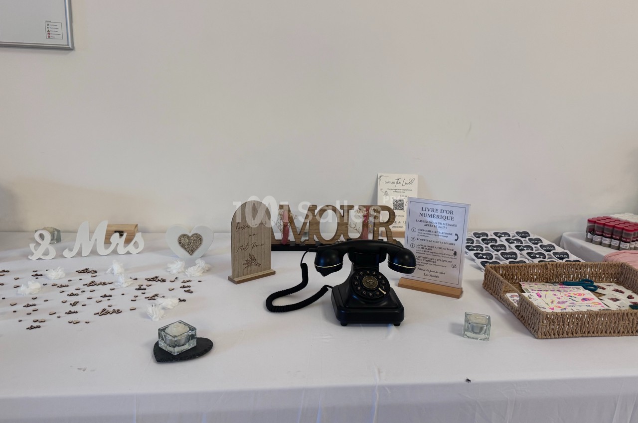 Table décorative avec un téléphone vintage, des accessoires de mariage et des boîtes de souvenirs sur une nappe blanche.