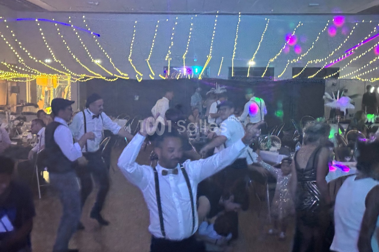 Des personnes dansent sous des guirlandes lumineuses dans une salle décorée pour une fête.