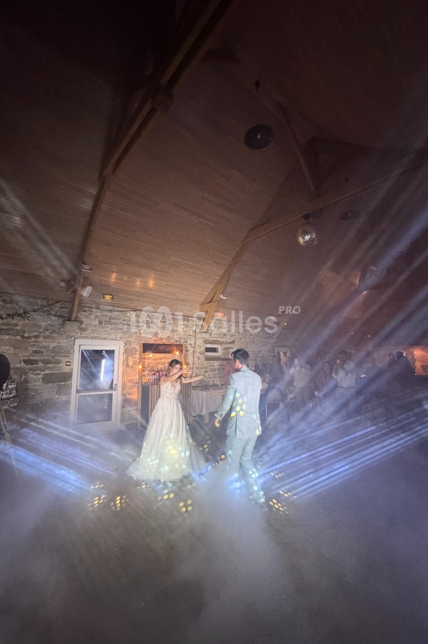 Un couple danse sous des jeux de lumière et de fumée dans une salle en pierre avec un plafond en bois.