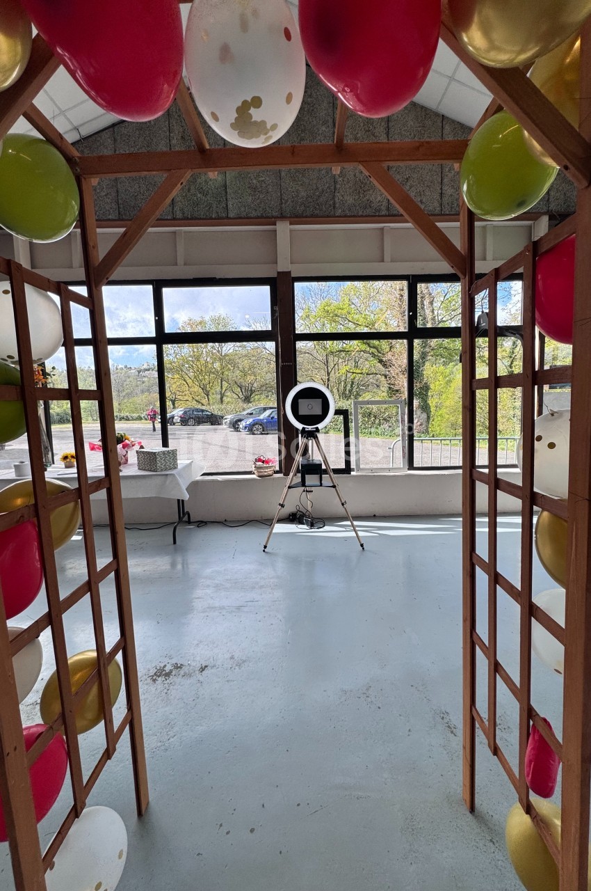 Structure en bois décorée de ballons colorés, avec un trépied et une lampe circulaire dans une pièce lumineuse.