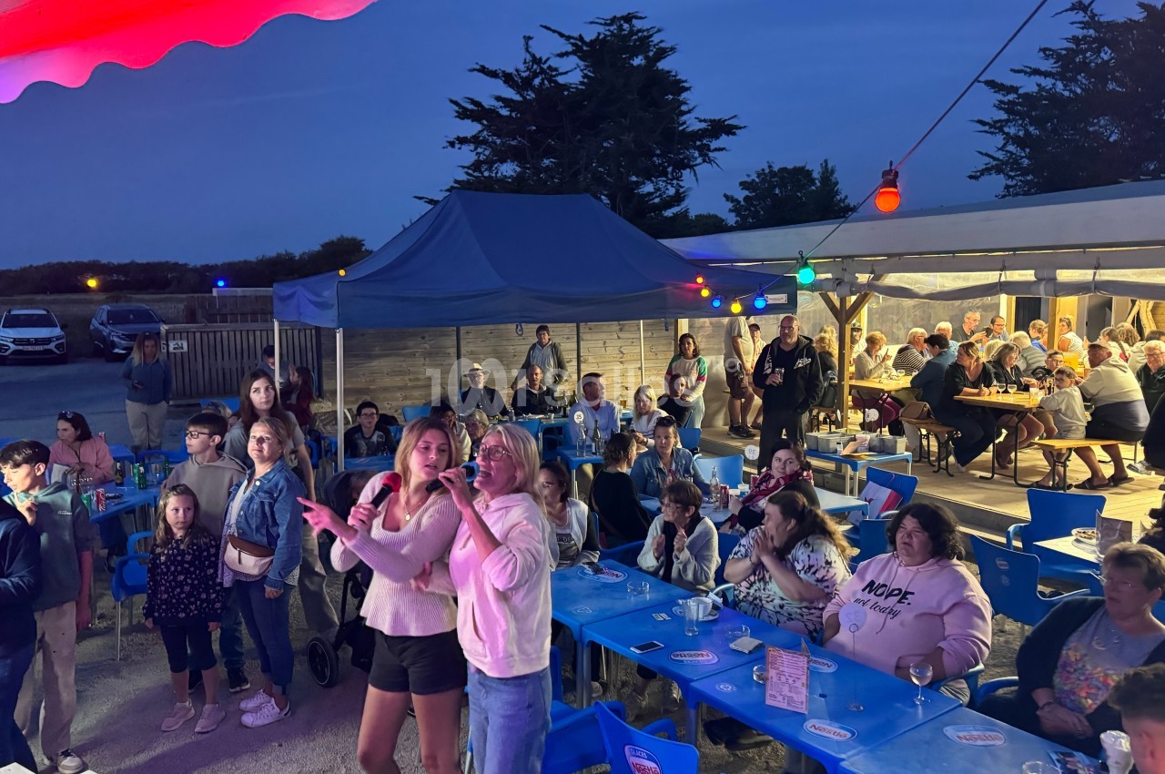 Des personnes participent à une soirée conviviale en plein air avec des tables, des lumières colorées et une ambiance…