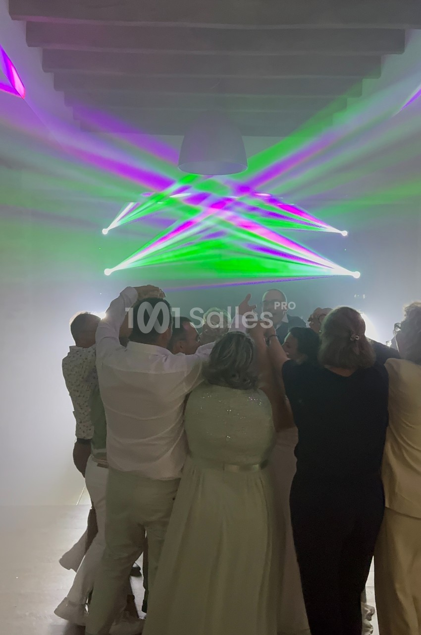 Groupe de personnes dansant sous des lumières colorées dans une salle sombre avec un plafond en bois.