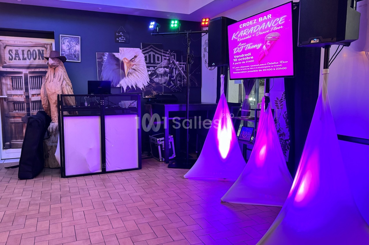 Salle de karaoké avec éclairage coloré, décorations sur le thème du Far West et panneau d'information lumineux.
