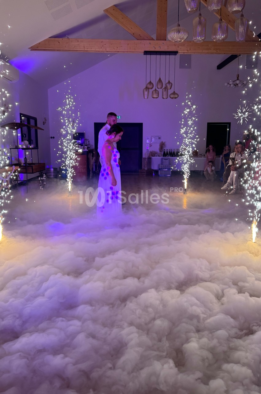 Un couple danse au milieu d'une salle éclairée, entouré de fumée au sol et de jets d'étincelles.
