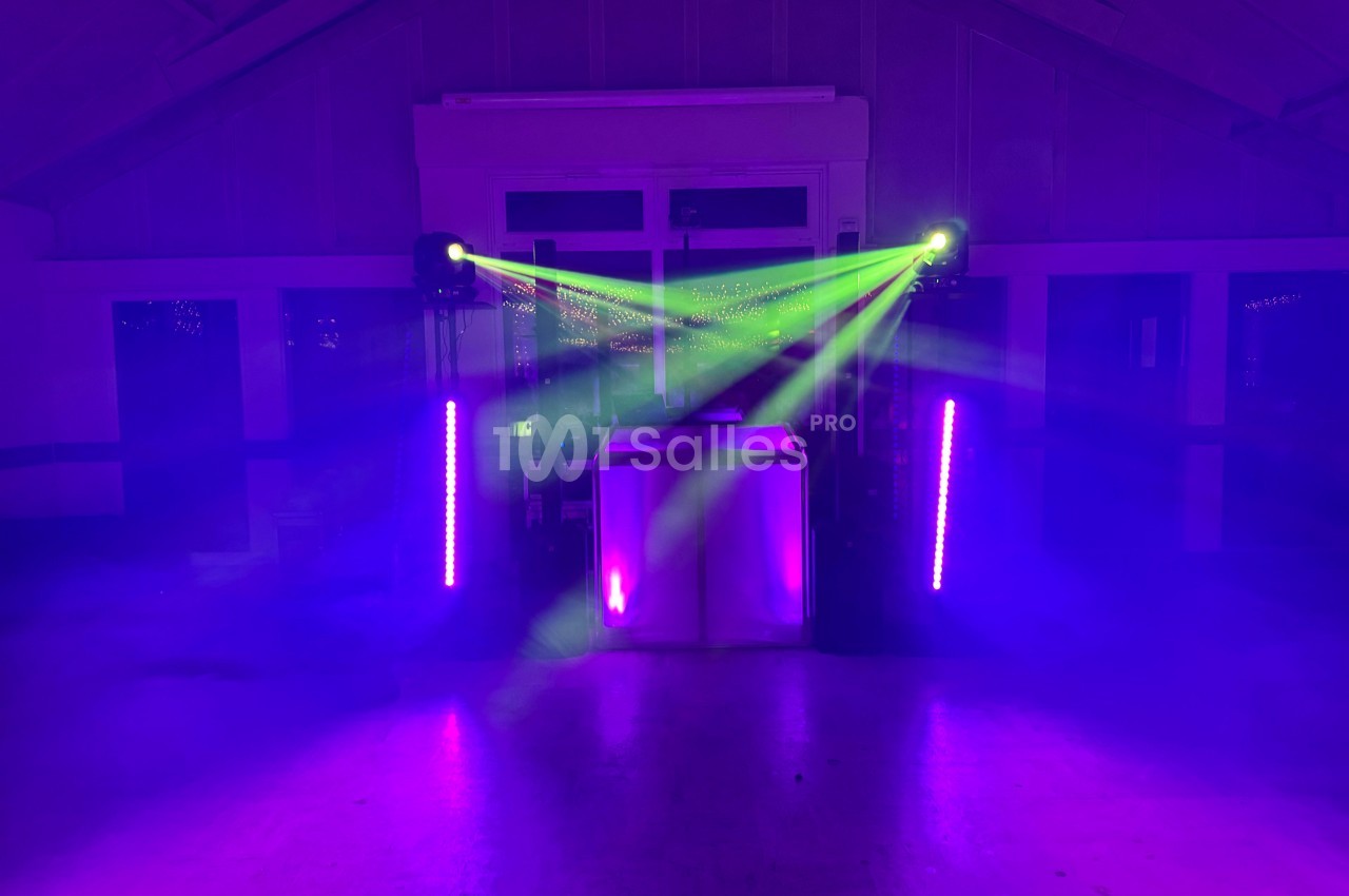 Jeux de lumières violettes et vertes éclairant une scène avec un équipement audio dans une salle sombre.