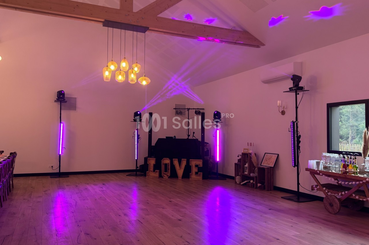 Salle de réception avec éclairage violet, piste de danse, lettres lumineuses ’LOVE’ et équipements audio.