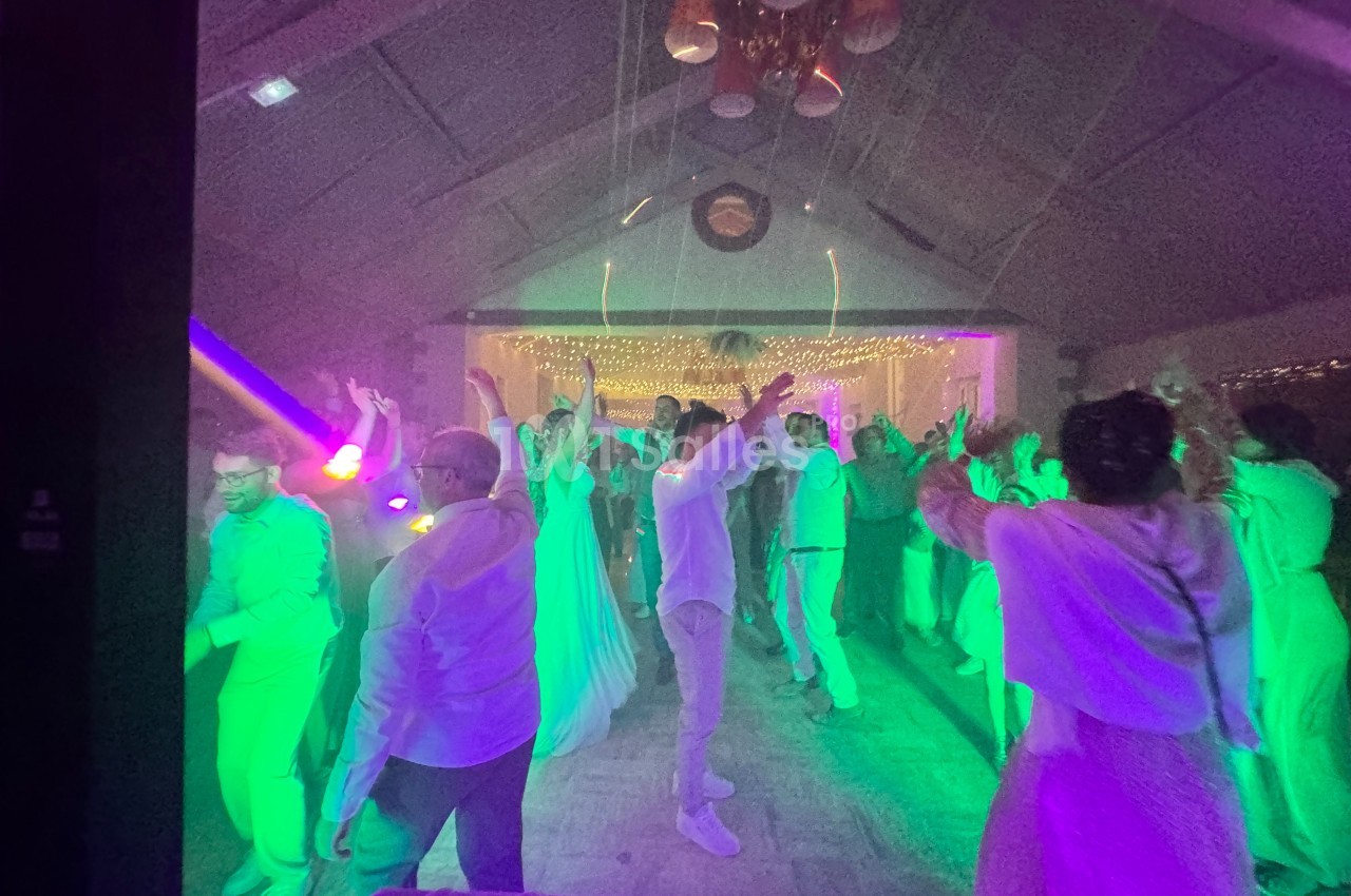 Personnes dansant sous des lumières colorées dans une salle décorée avec des guirlandes lumineuses.