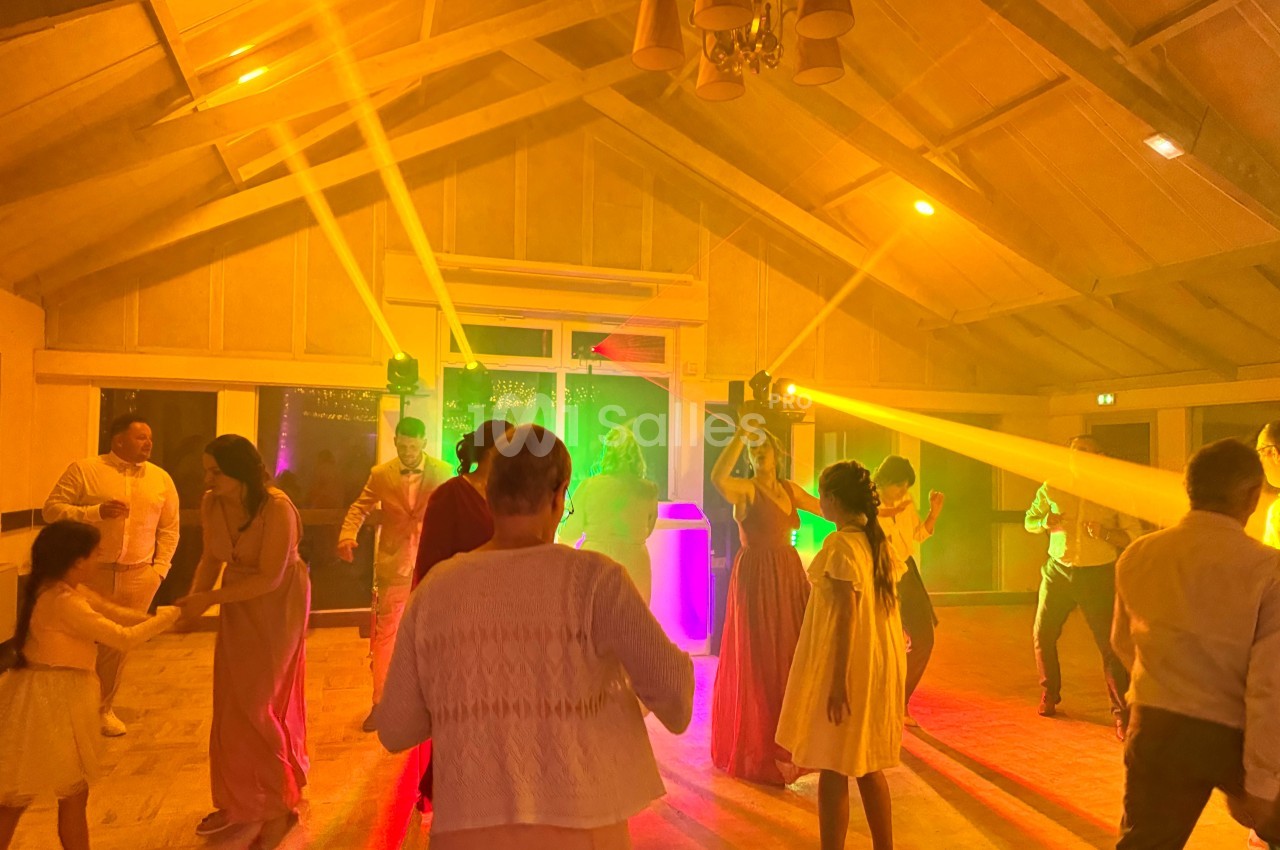 Des personnes dansent dans une salle éclairée par des lumières colorées, créant une ambiance festive.