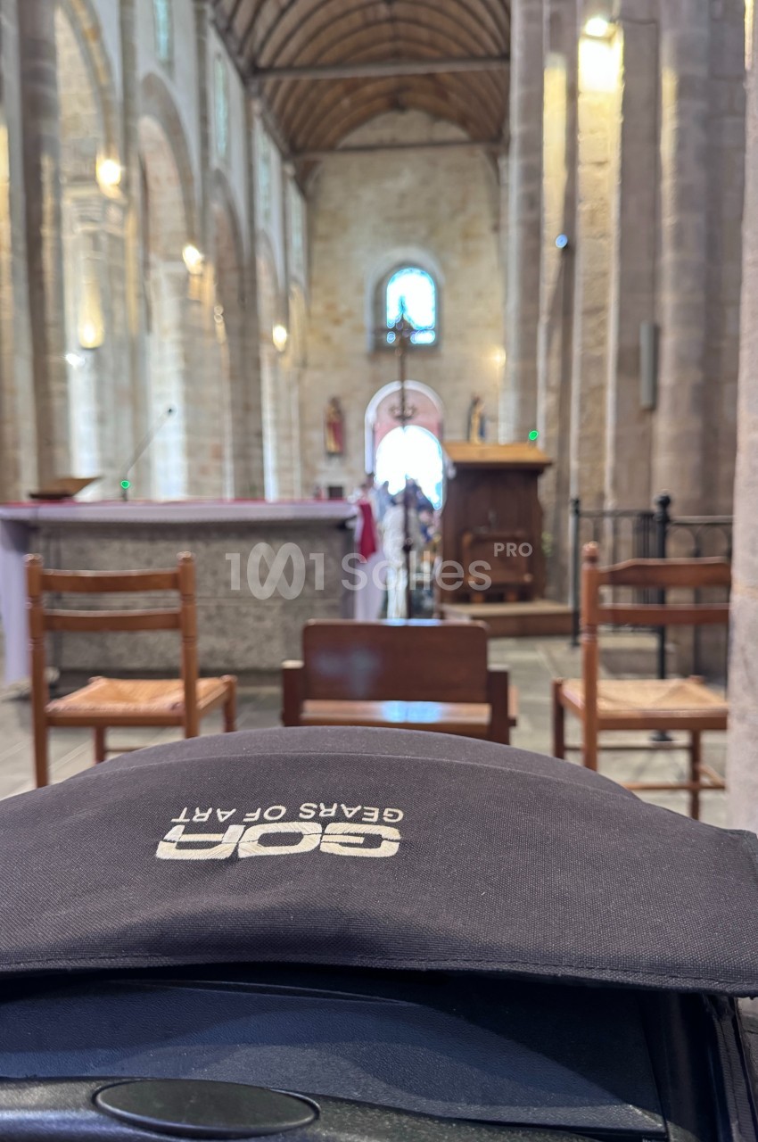 Intérieur d'une église avec des chaises en bois, un autel et une voûte en pierre illuminée par la lumière naturelle.