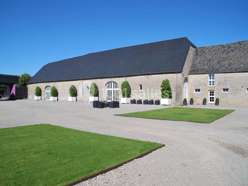 Cour extérieure avec pelouses rectangulaires, graviers et bâtiment en pierre à toit d'ardoise sous un ciel bleu.