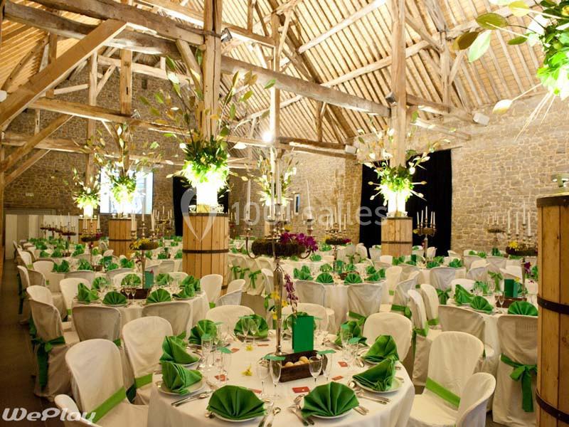 Salle de réception décorée avec des tables rondes, nappes blanches, serviettes vertes et arrangements floraux.