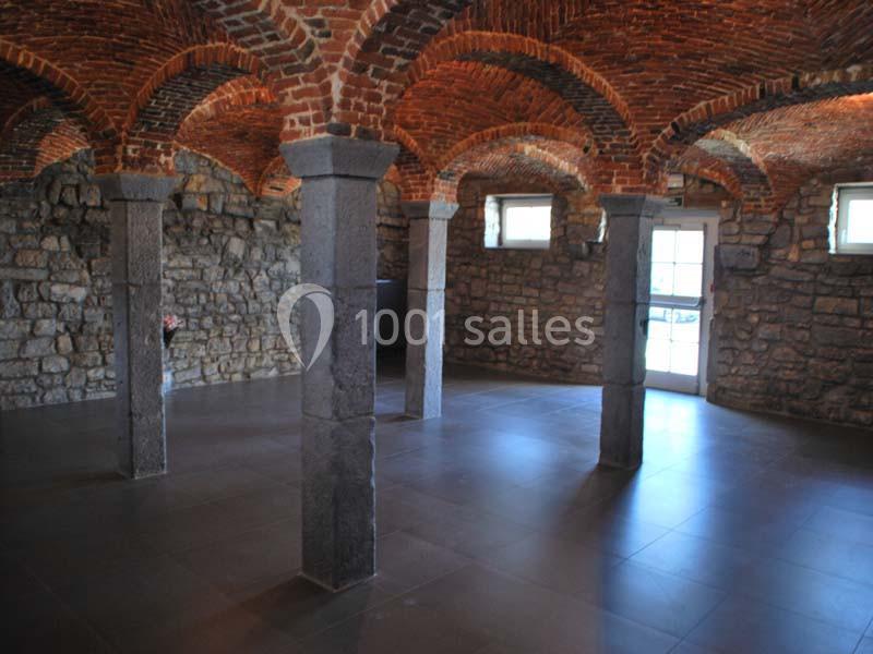 Salle voûtée en briques et pierres, éclairée par des fenêtres et une porte, avec des colonnes en pierre.