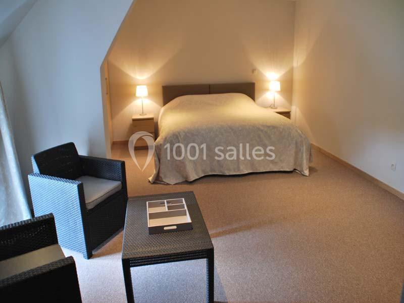Chambre avec lit double, deux lampes de chevet, fauteuils en rotin et table basse sur un sol en moquette beige.