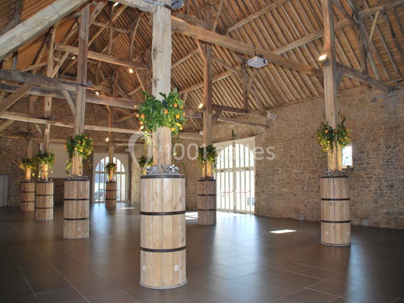 Salle spacieuse avec charpente en bois apparente, piliers décorés de plantes et murs en pierre.
