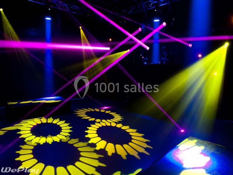 Jeux de lumières colorées avec faisceaux roses et jaunes projetés sur une piste de danse sombre.