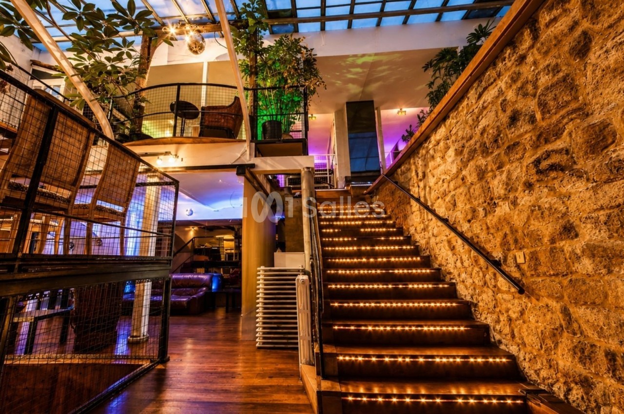 Escalier en bois éclairé par des lumières intégrées, entouré de murs en pierre et de plantes dans un espace moderne.