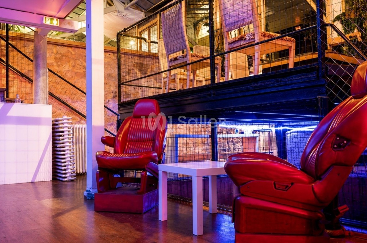 Deux fauteuils rouges devant une table basse blanche dans un espace intérieur au design industriel avec éclairage coloré.