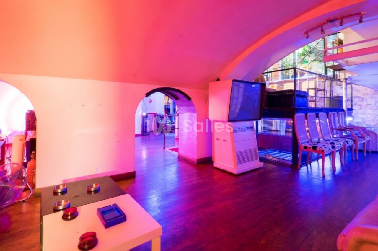 Salle colorée avec éclairage rose et violet, équipée de fauteuils, tables basses et écrans, dans un espace voûté.