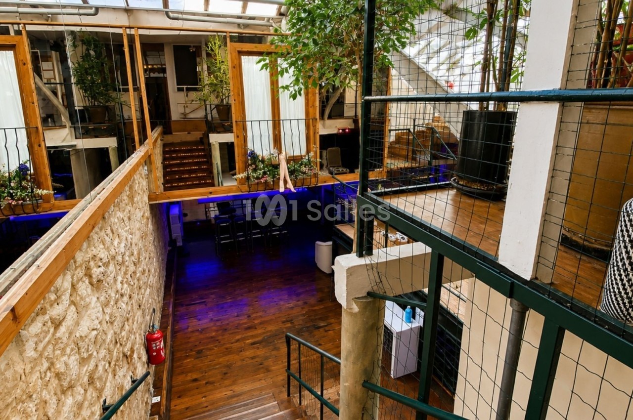 Intérieur d'un espace lumineux avec mezzanine, murs en pierre, plantes et parquet en bois.
