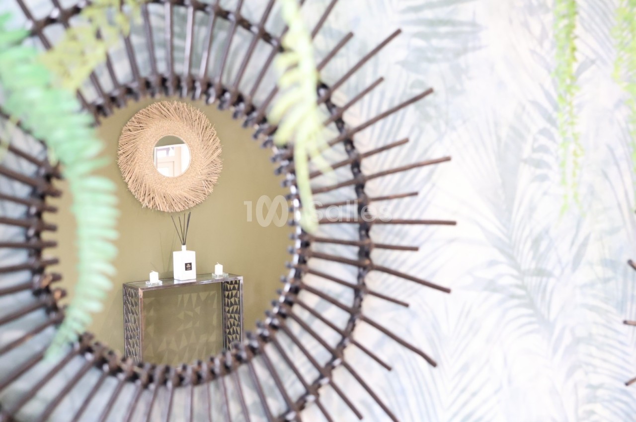 Reflet d'un miroir en rotin montrant une console avec un diffuseur de parfum et deux bougies, décorée de plantes.