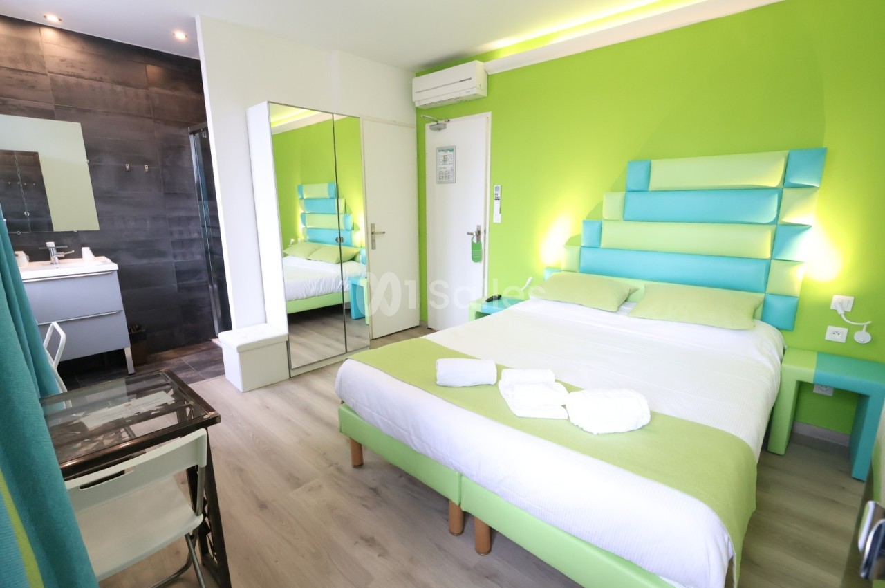 Chambre d'hôtel moderne avec lit double, murs verts, salle de bain attenante et mobilier contemporain.