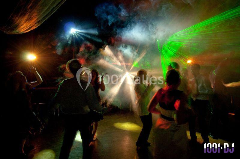 Des personnes dansent dans une salle sombre éclairée par des jeux de lumière colorés et des faisceaux laser.