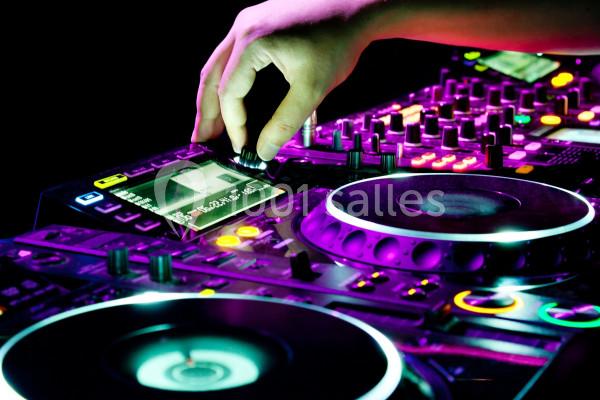 Main ajustant un bouton sur une table de mixage DJ éclairée par des lumières colorées.