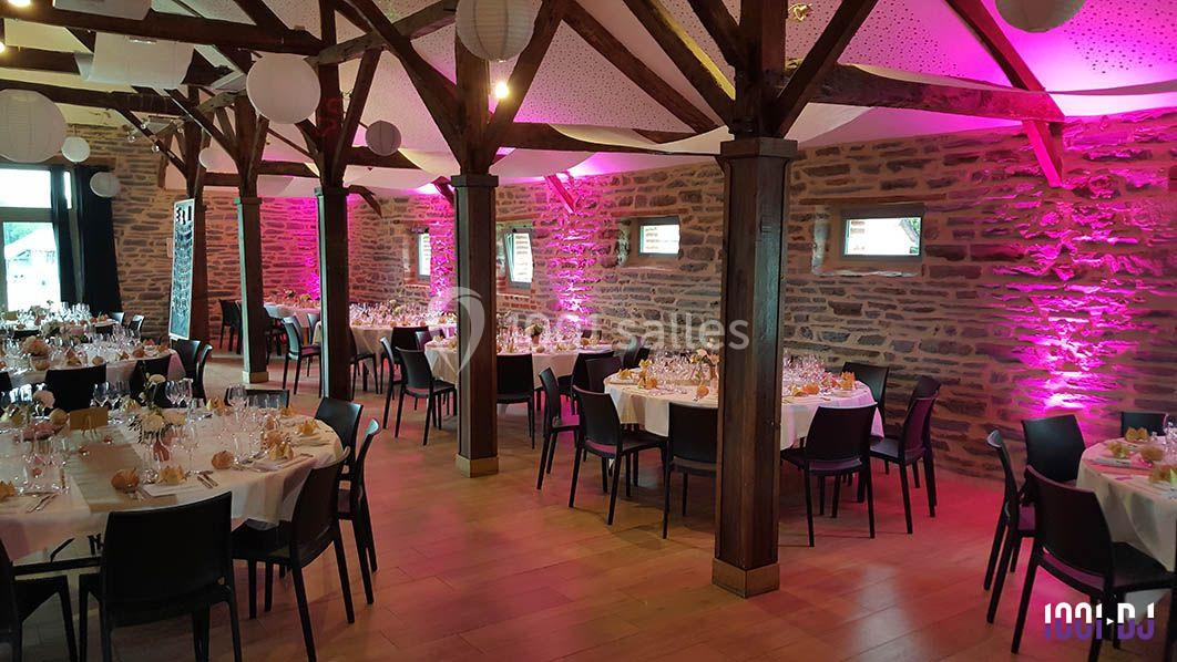 Salle de réception avec murs en pierre, poutres apparentes et tables rondes dressées pour un événement.