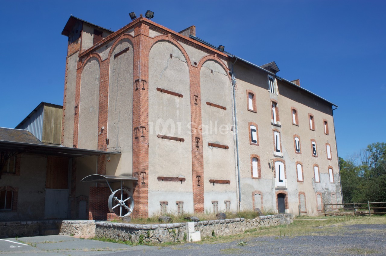 Bâtiment ancien en briques et crépi, avec des fenêtres murées, situé dans un environnement rural par temps ensoleillé.