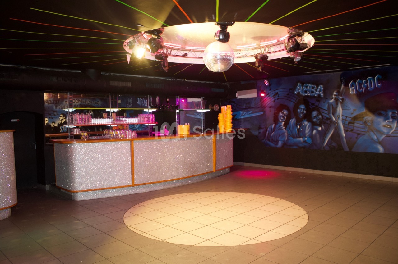 Salle de danse avec piste circulaire éclairée, bar scintillant et fresque murale colorée sous des lumières tamisées.