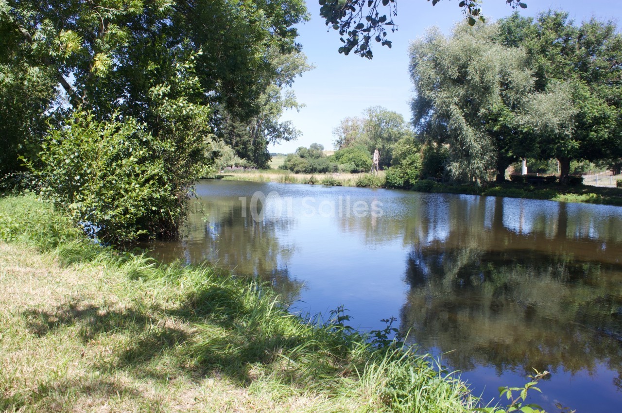 Plan d'eau calme entouré d'arbres et de végétation, reflétant le ciel bleu par une journée ensoleillée.