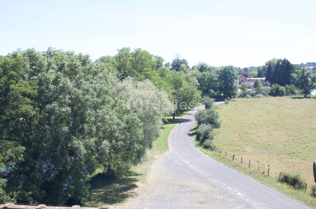Route de campagne bordée d'arbres et de prairies, menant à un petit village sous un ciel dégagé.