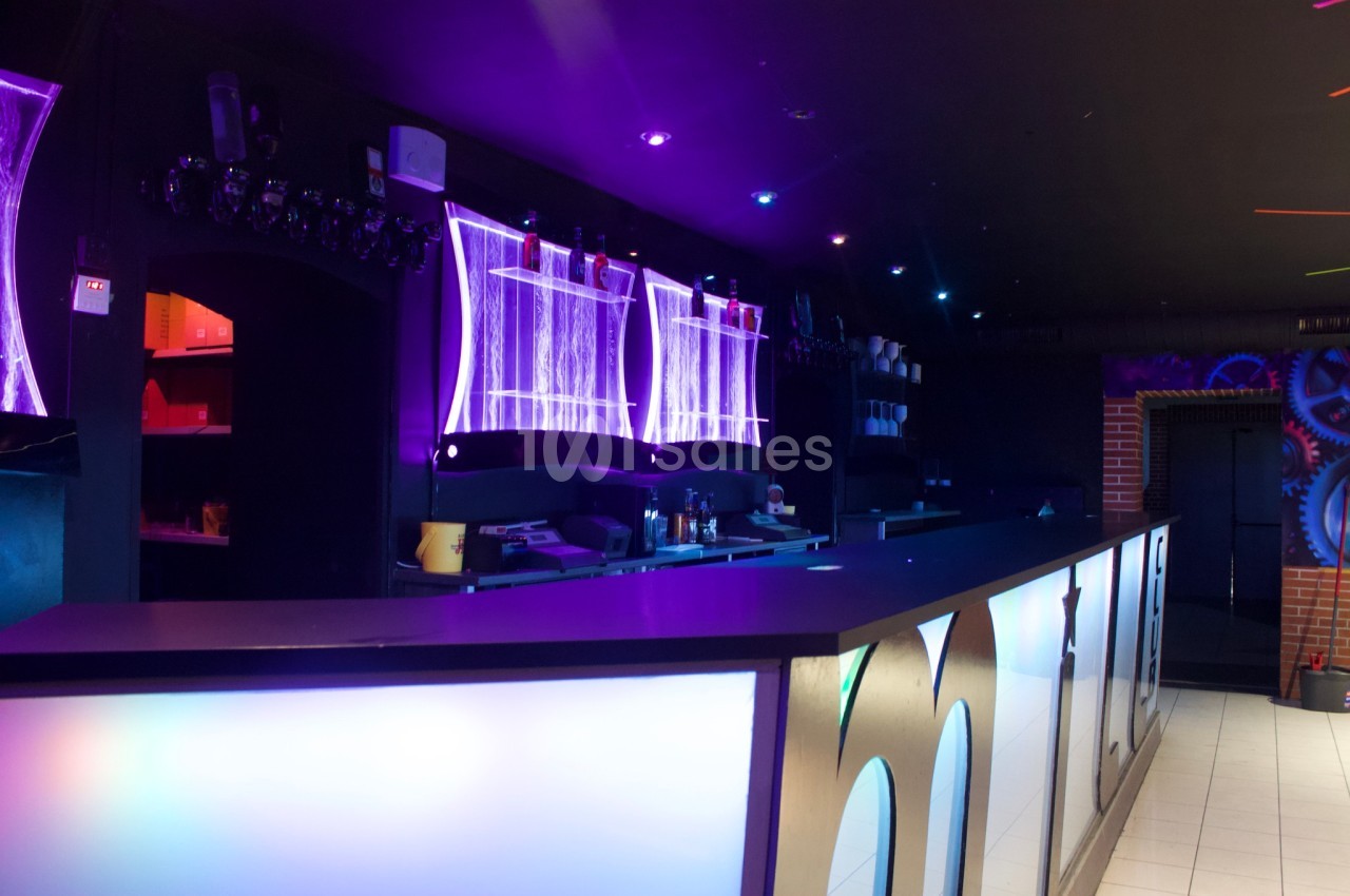 Comptoir de bar moderne éclairé par des néons violets et bleus dans une ambiance sombre.
