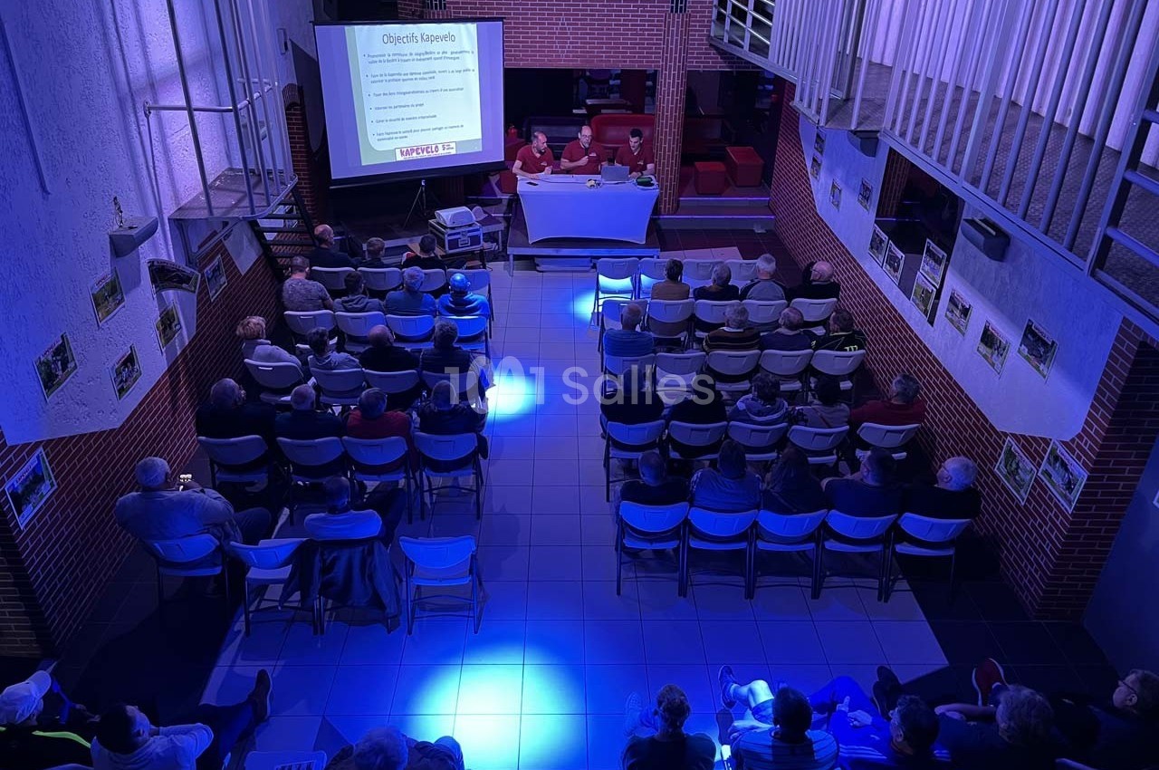 Salle de conférence avec des participants assis, regardant une présentation projetée sur un écran.