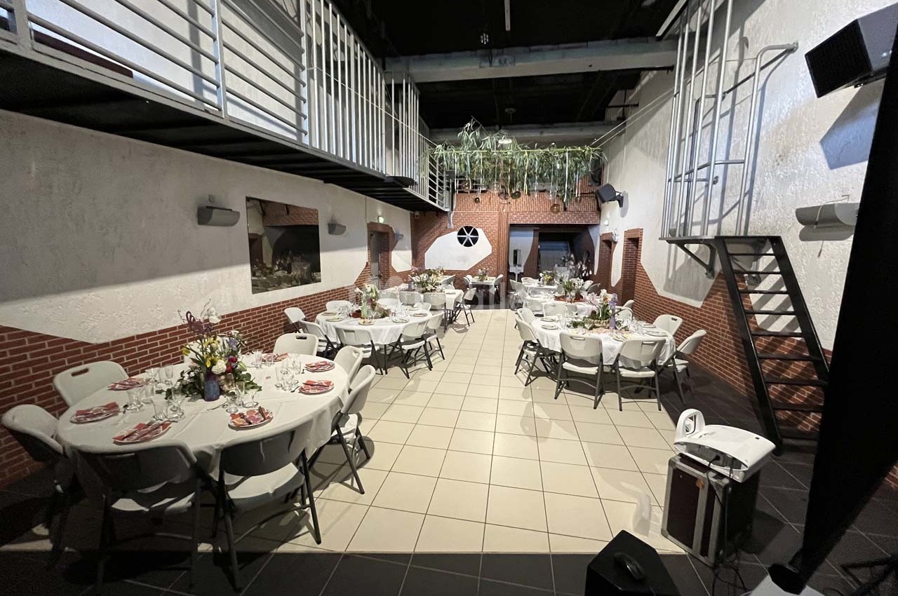 Salle de réception décorée avec des tables rondes dressées, des chaises blanches et des plantes suspendues.