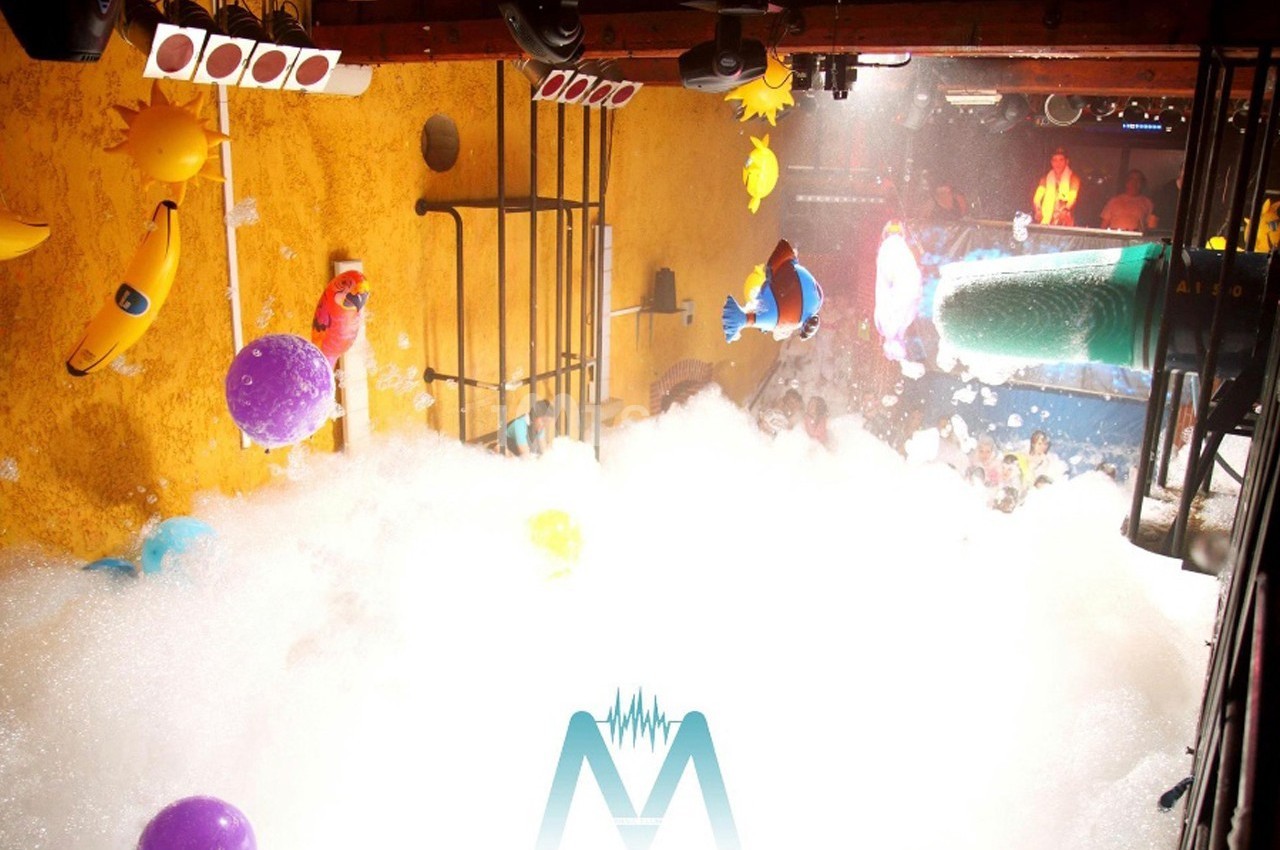 Salle de fête remplie de mousse, décorations colorées suspendues et éclairage festif.