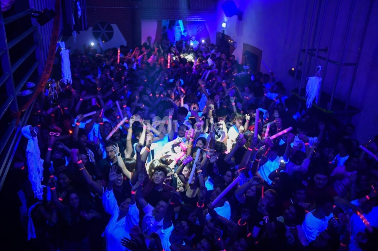 Foule dans une discothèque sombre avec des lumières bleues et des bâtons lumineux roses.