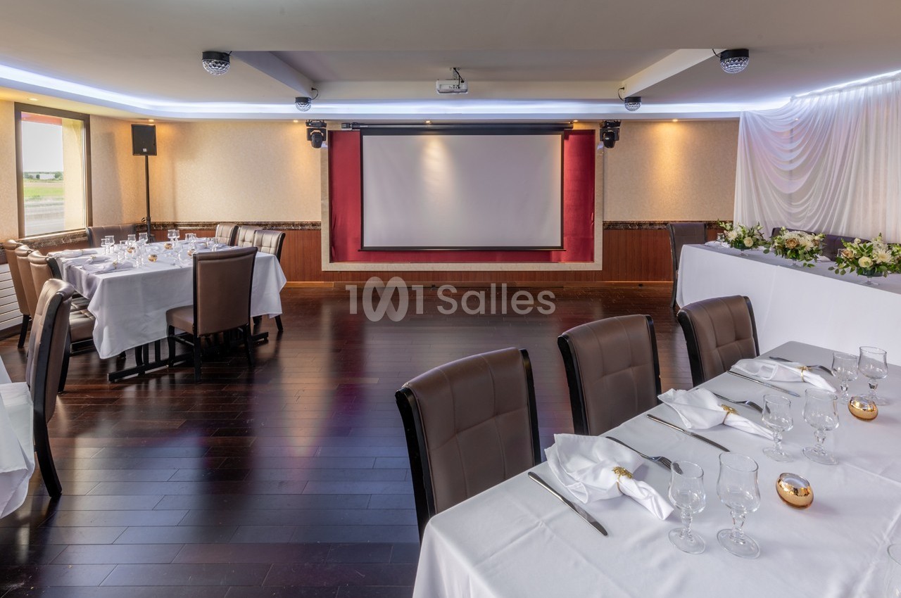 Salle de réception avec tables dressées, écran de projection et décoration lumineuse.