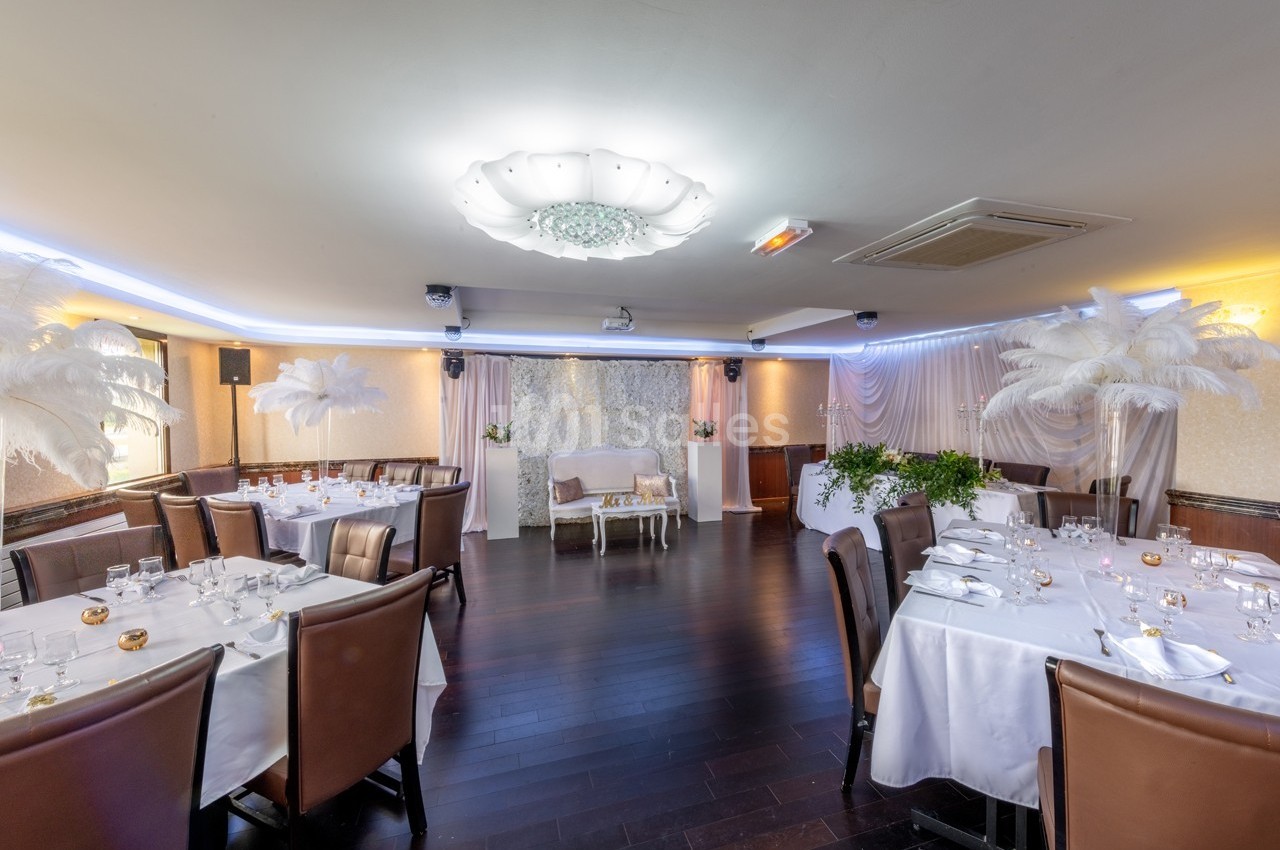 Salle de réception élégamment décorée avec tables dressées, fauteuils en cuir et ornements de plumes blanches.