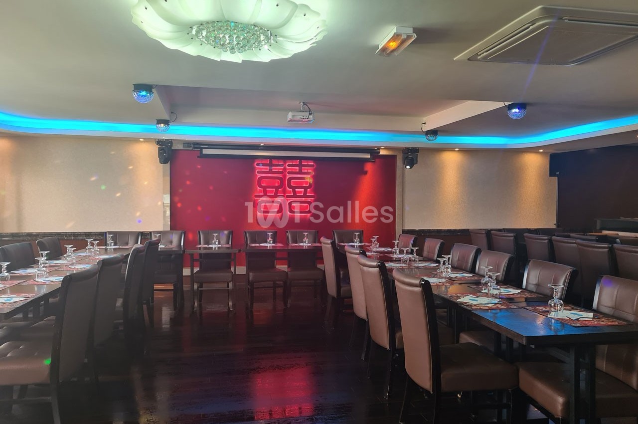 Salle de restaurant moderne avec tables dressées, chaises en cuir marron et éclairage coloré sur un mur décoratif rouge.