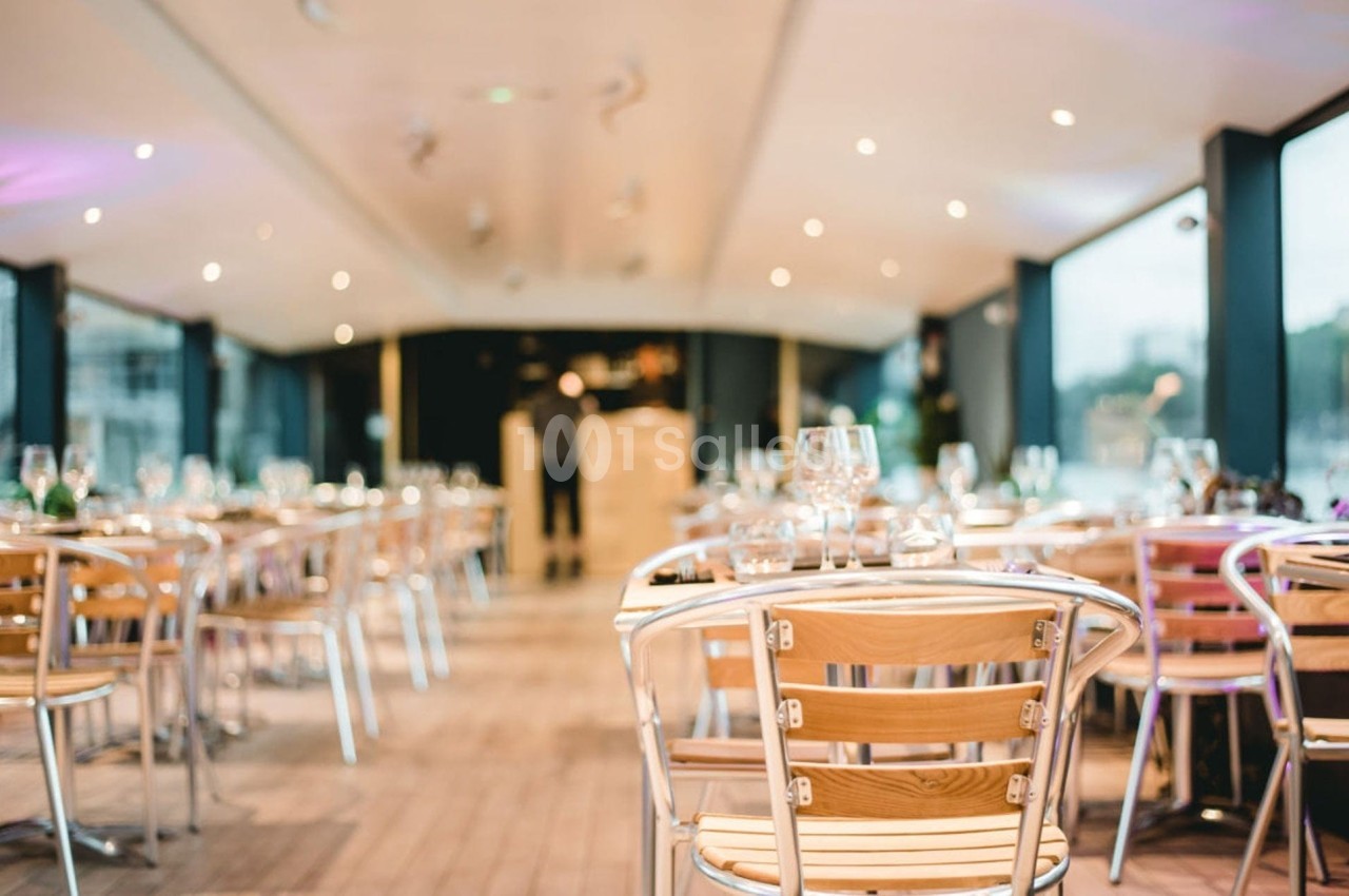 Salle de restaurant lumineuse avec des tables en bois et des chaises métalliques, vue sur de grandes baies vitrées.