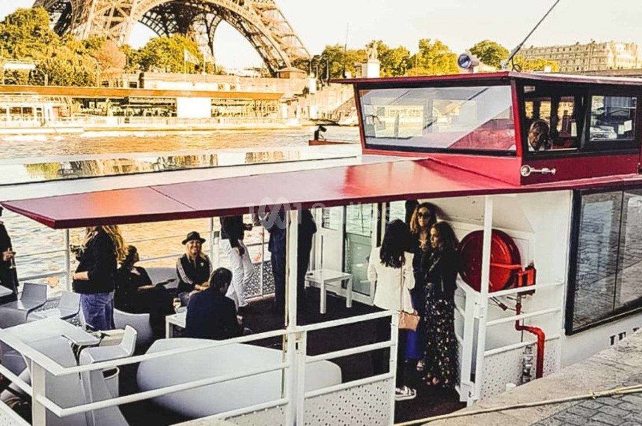 Bateau amarré sur la Seine avec des passagers à bord, la tour Eiffel visible en arrière-plan.