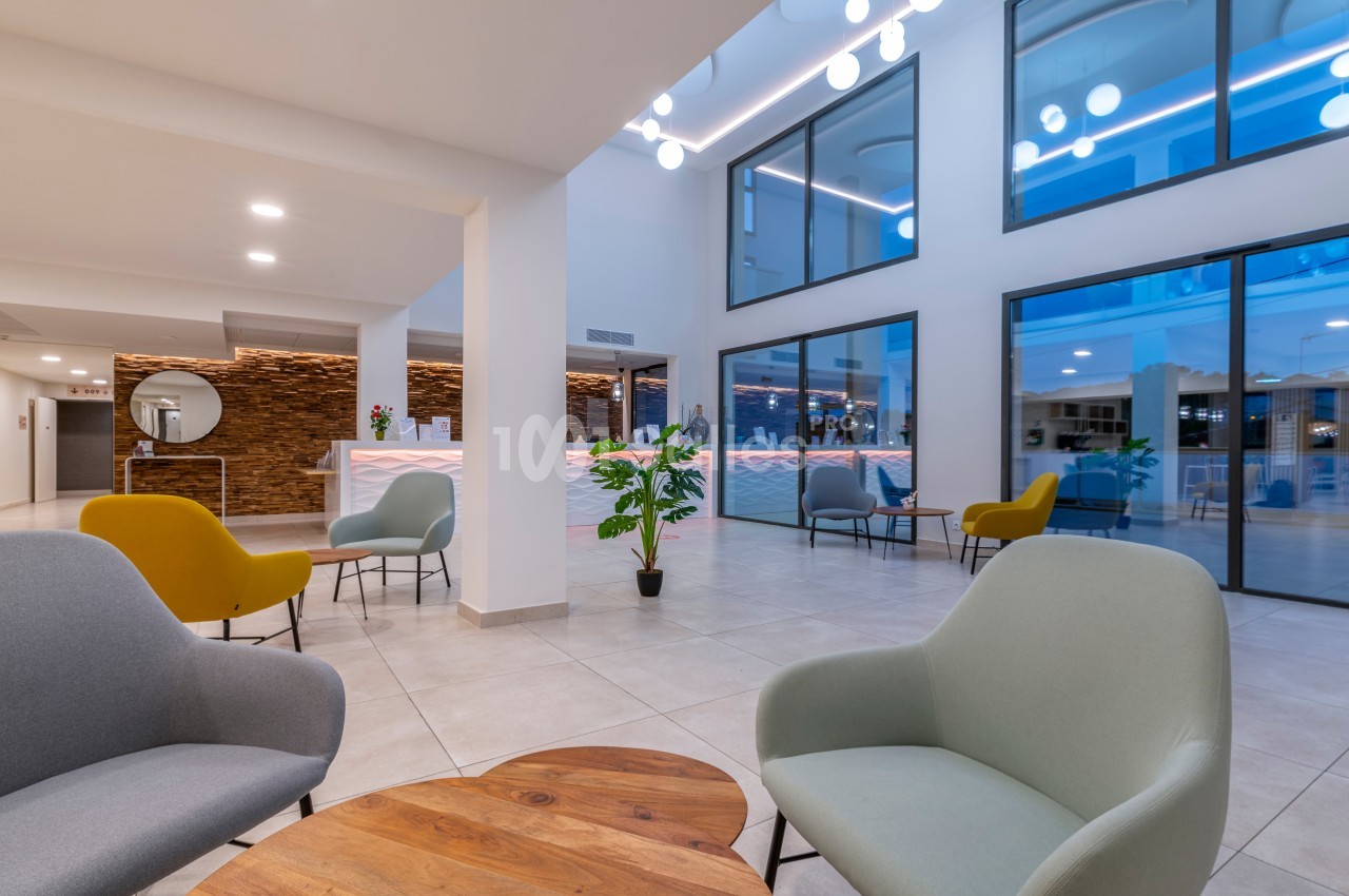 Espace lounge moderne avec fauteuils colorés, table basse en bois et grande baie vitrée donnant sur l'extérieur.