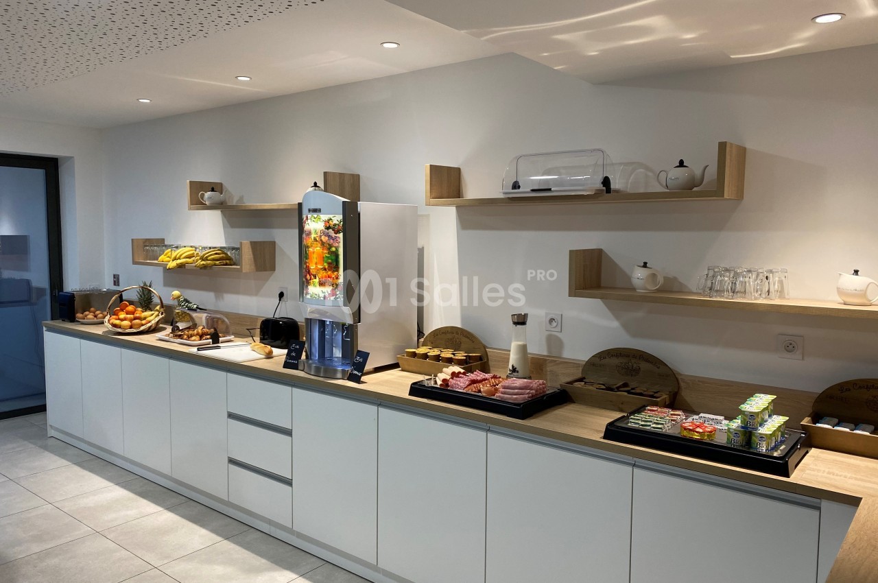 Buffet de petit-déjeuner avec fruits, viennoiseries, charcuterie, boissons et vaisselle dans une salle lumineuse.