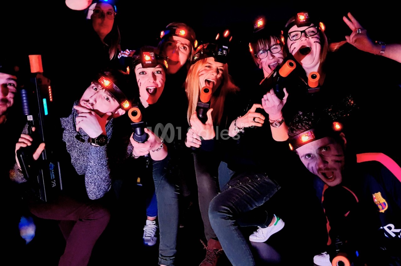 Un groupe de personnes souriantes joue au laser game dans un environnement sombre, portant des équipements lumineux.